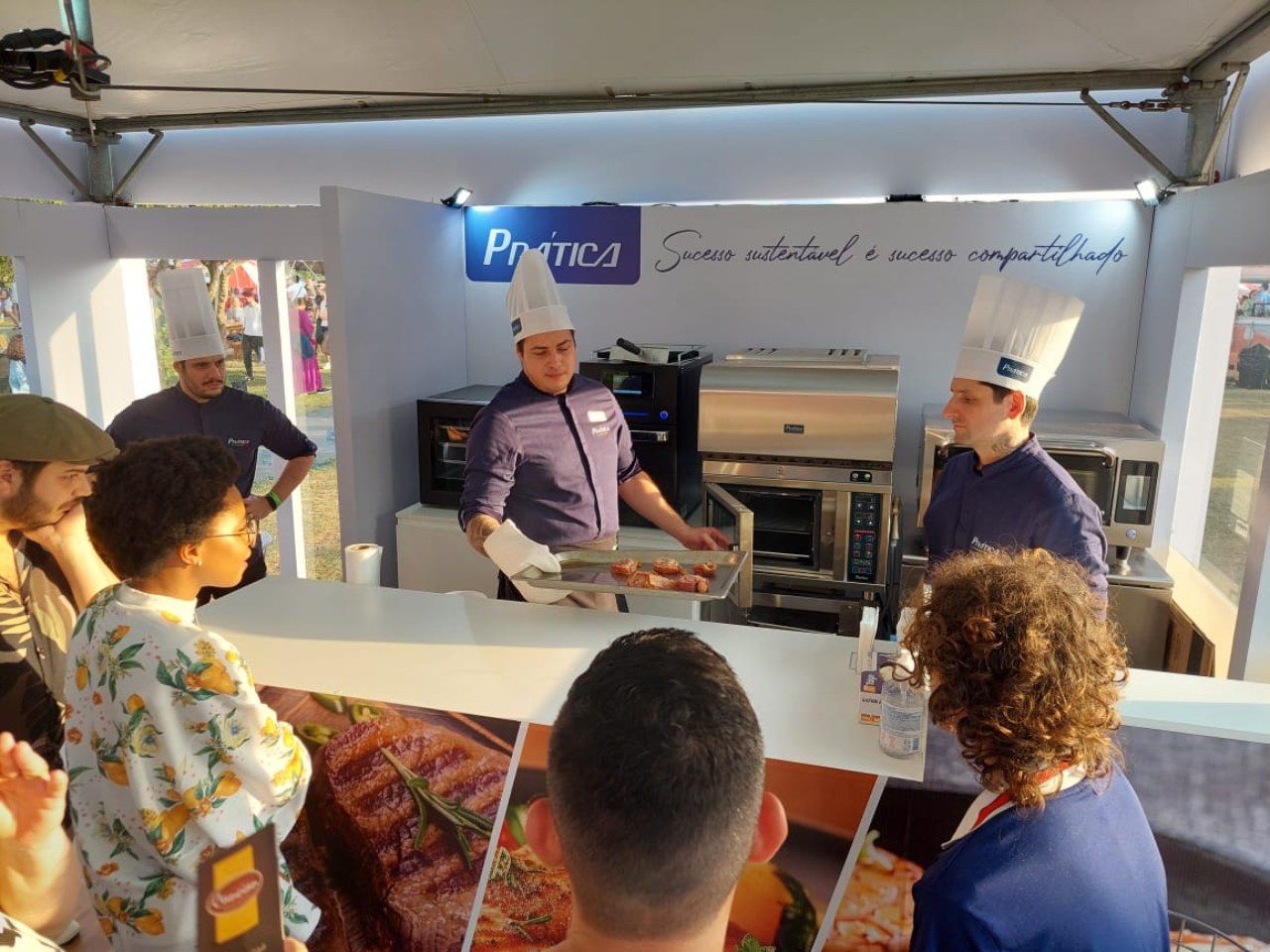 Um grupo de pessoas em pé ao redor de um balcão com uma placa que diz pratica