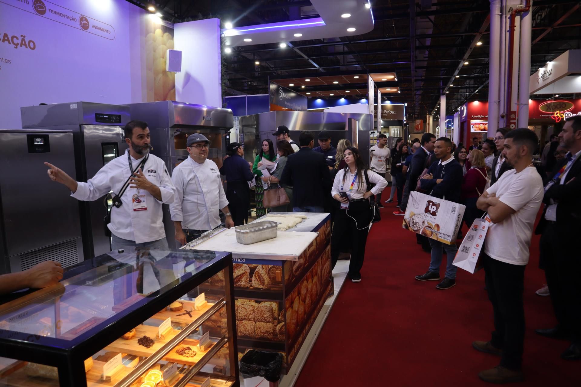 Um grupo de pessoas está em volta de uma vitrine em uma padaria.