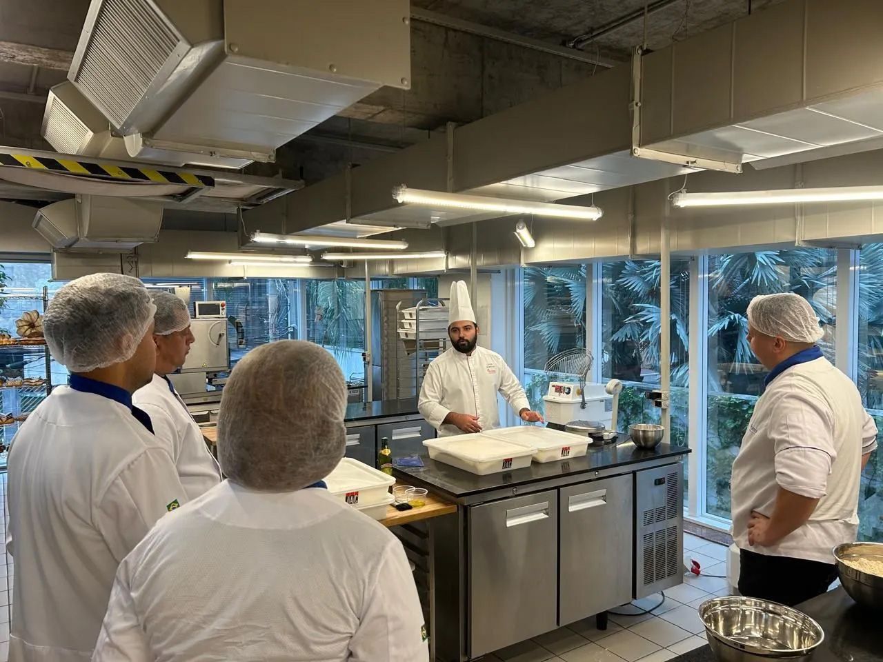 Um grupo de chefs estão em uma cozinha conversando entre si.
