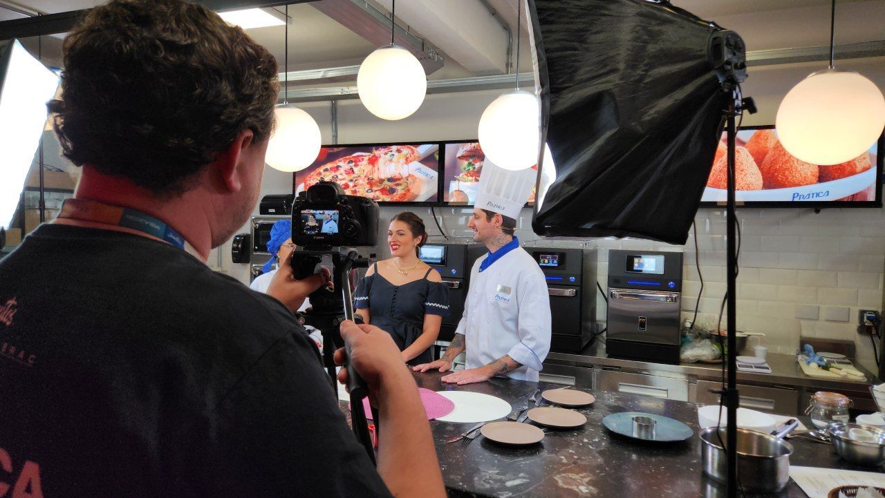 Um homem está tirando uma foto de um chef e uma mulher na cozinha.