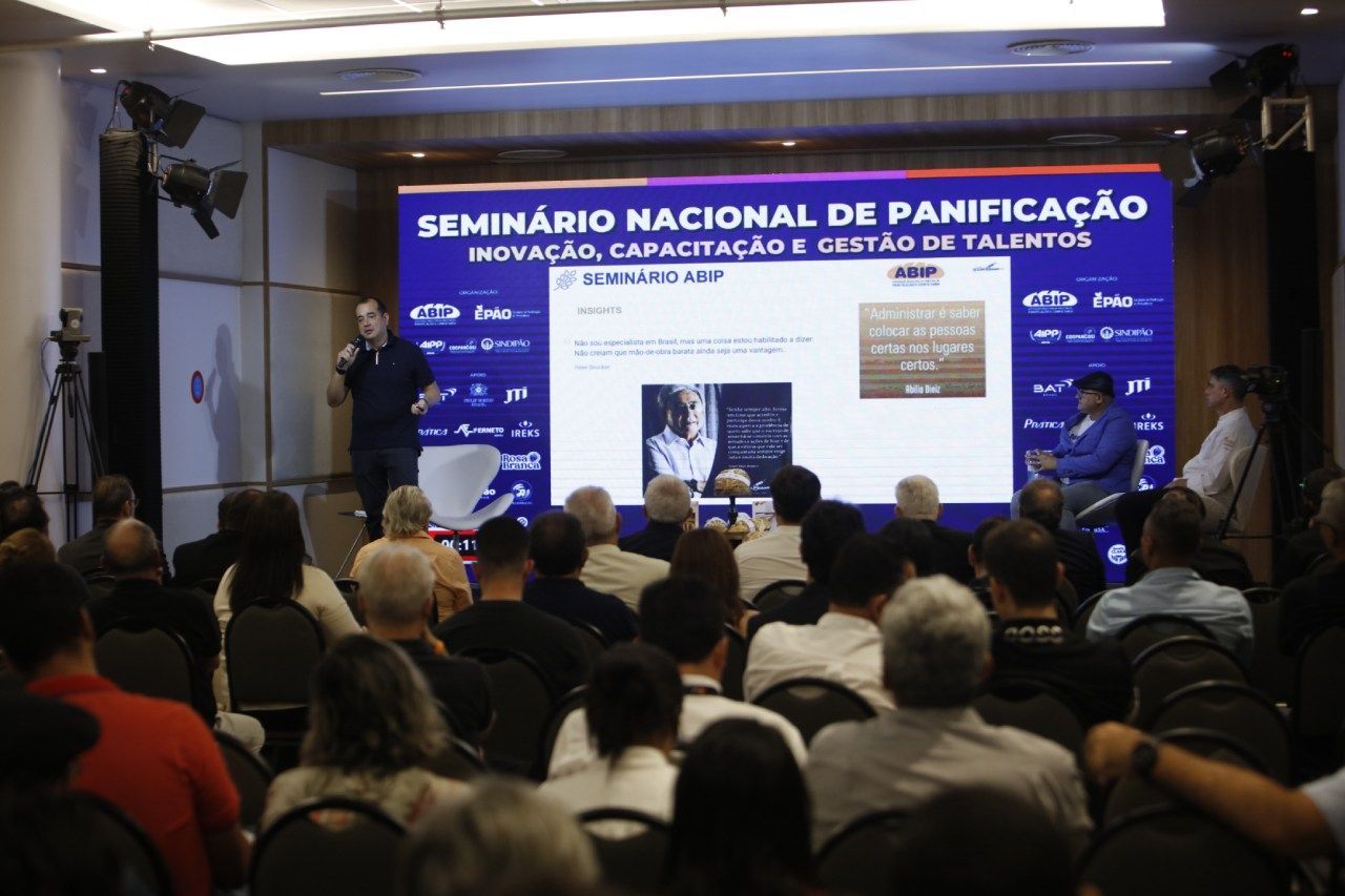 A group of people are sitting in front of a screen that says seminario nacional de panificação