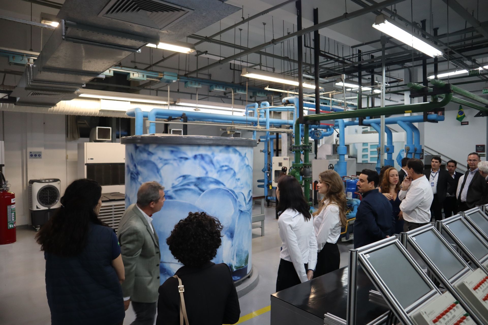 Pessoas em visita guiada a um laboratório, examinando equipamentos e o sistema de purificação de água.