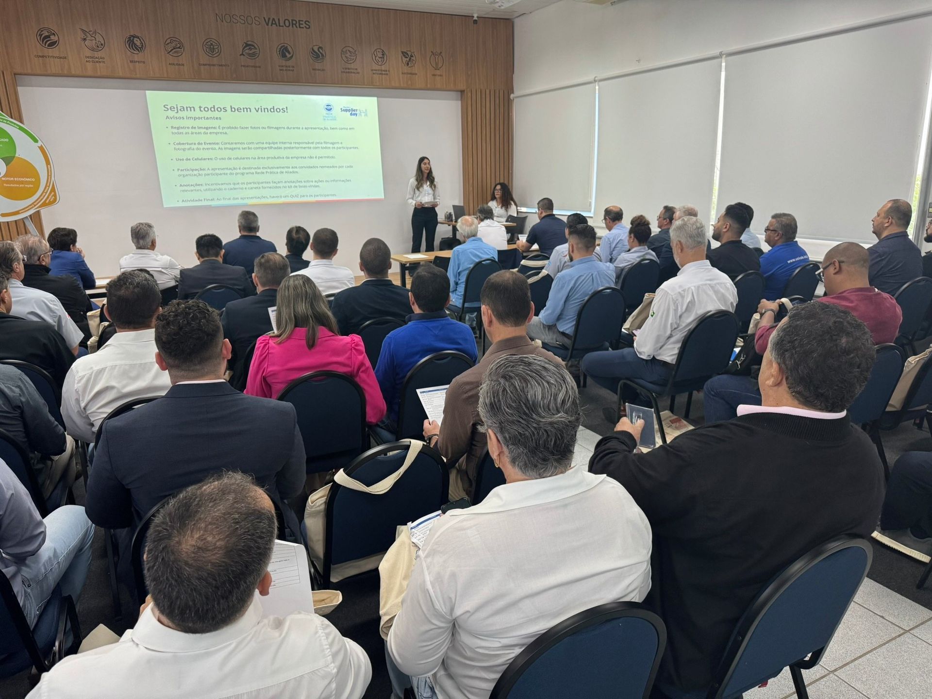 Um grupo de pessoas está sentado em cadeiras em frente a uma tela de projetor.