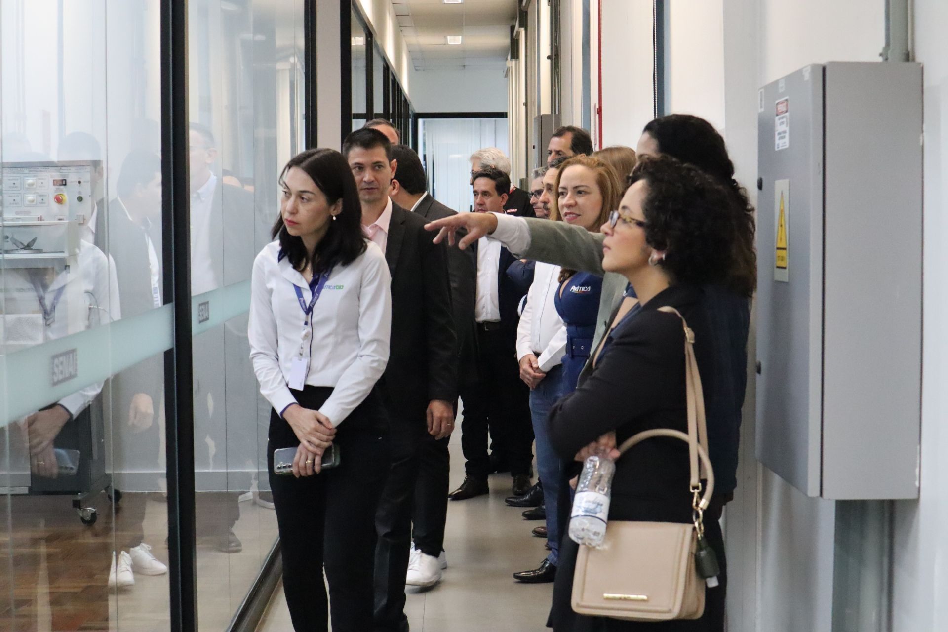 Grupo de pessoas observando um laboratório através de uma parede de vidro. Um homem aponta, enquanto os outros observam.