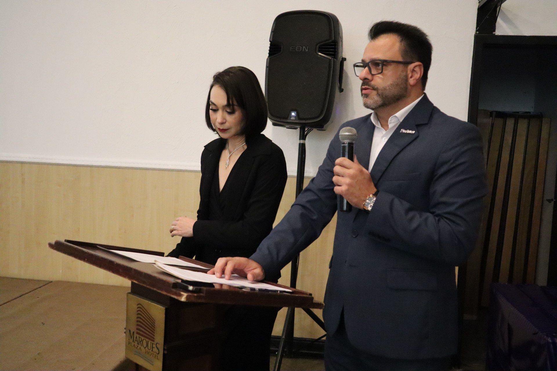 Um homem e uma mulher estão em um pódio falando em microfones.