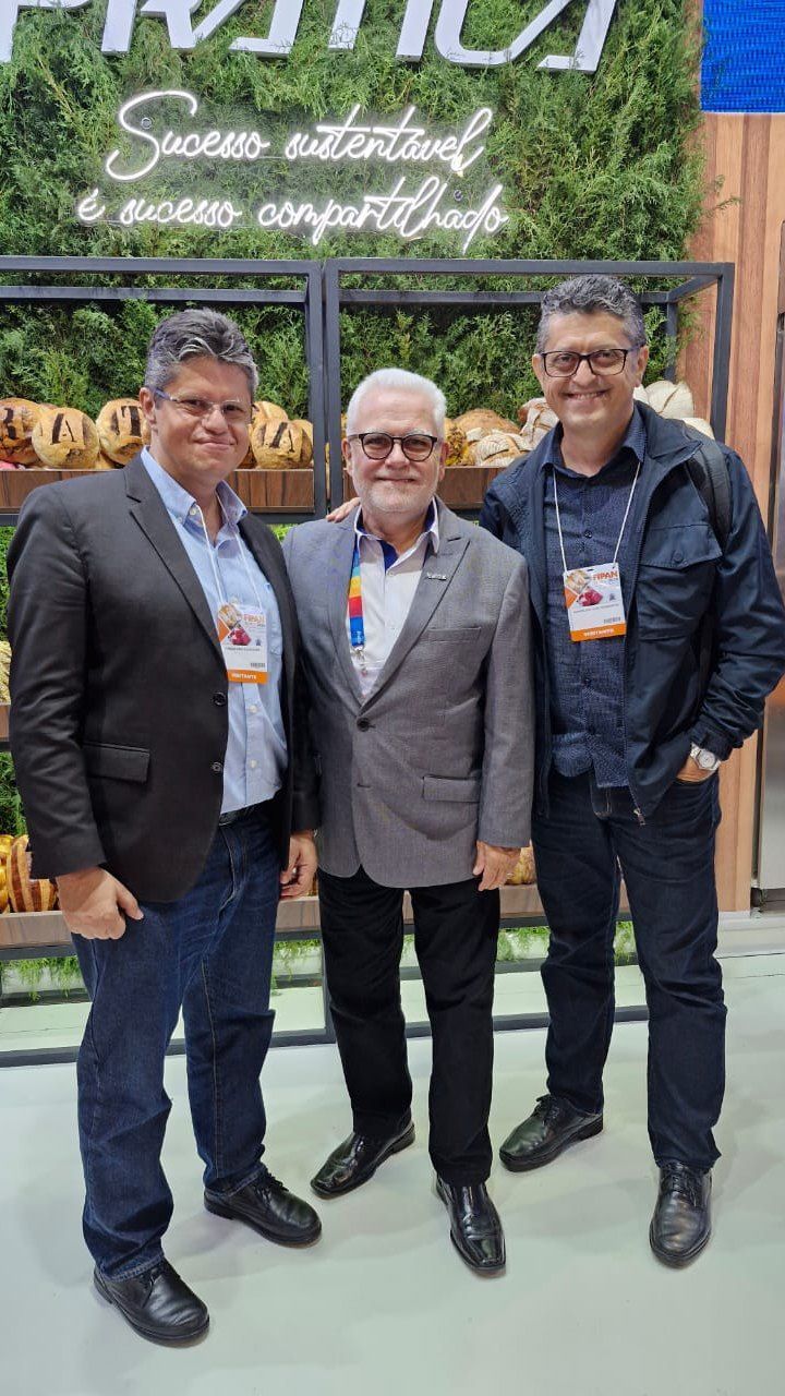 Três homens estão posando para uma foto em frente a uma parede de plantas.