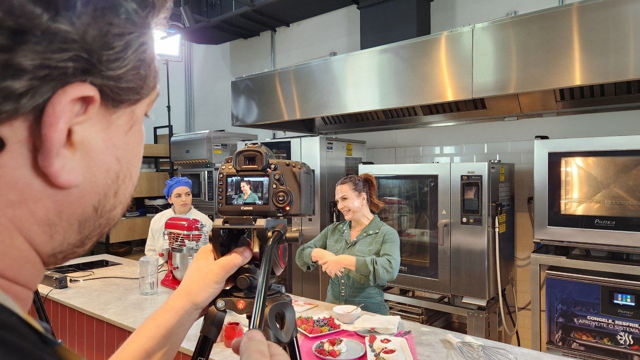 Um homem está tirando uma foto de uma mulher na cozinha com uma câmera.