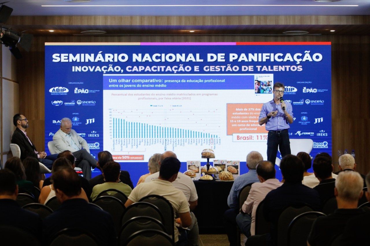 Um homem está fazendo uma apresentação para um grupo de pessoas em frente a uma tela grande.