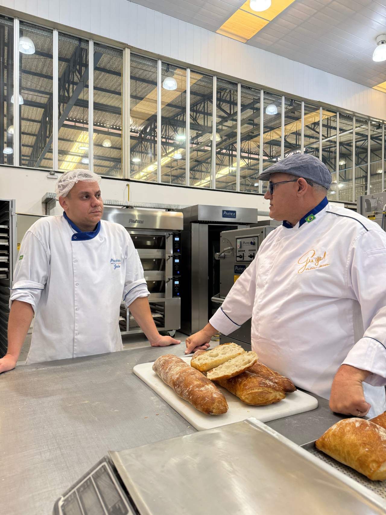 Dois chefs estão parados um ao lado do outro em uma padaria.