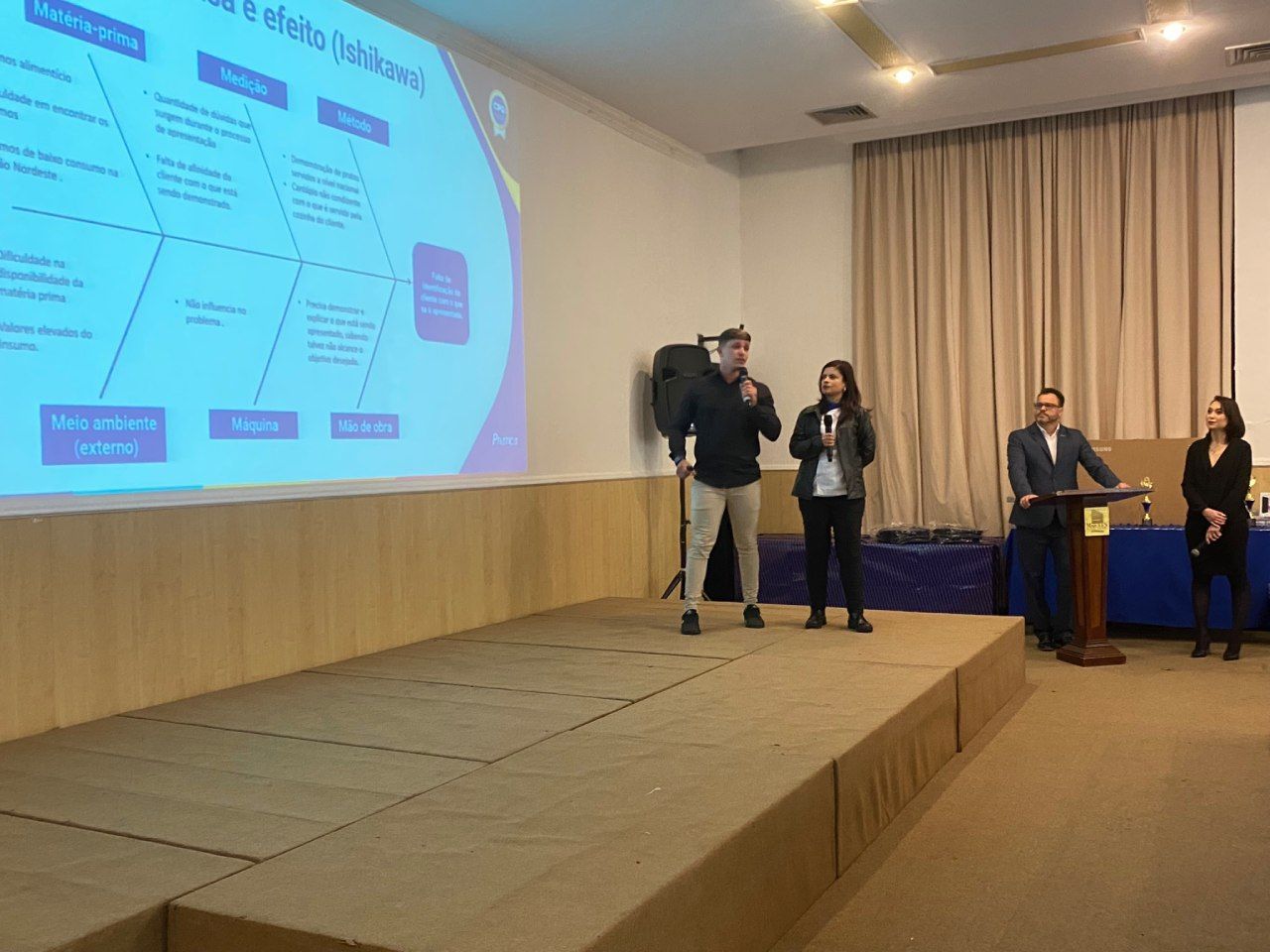 Um grupo de pessoas está em pé em um palco em frente a uma tela grande.