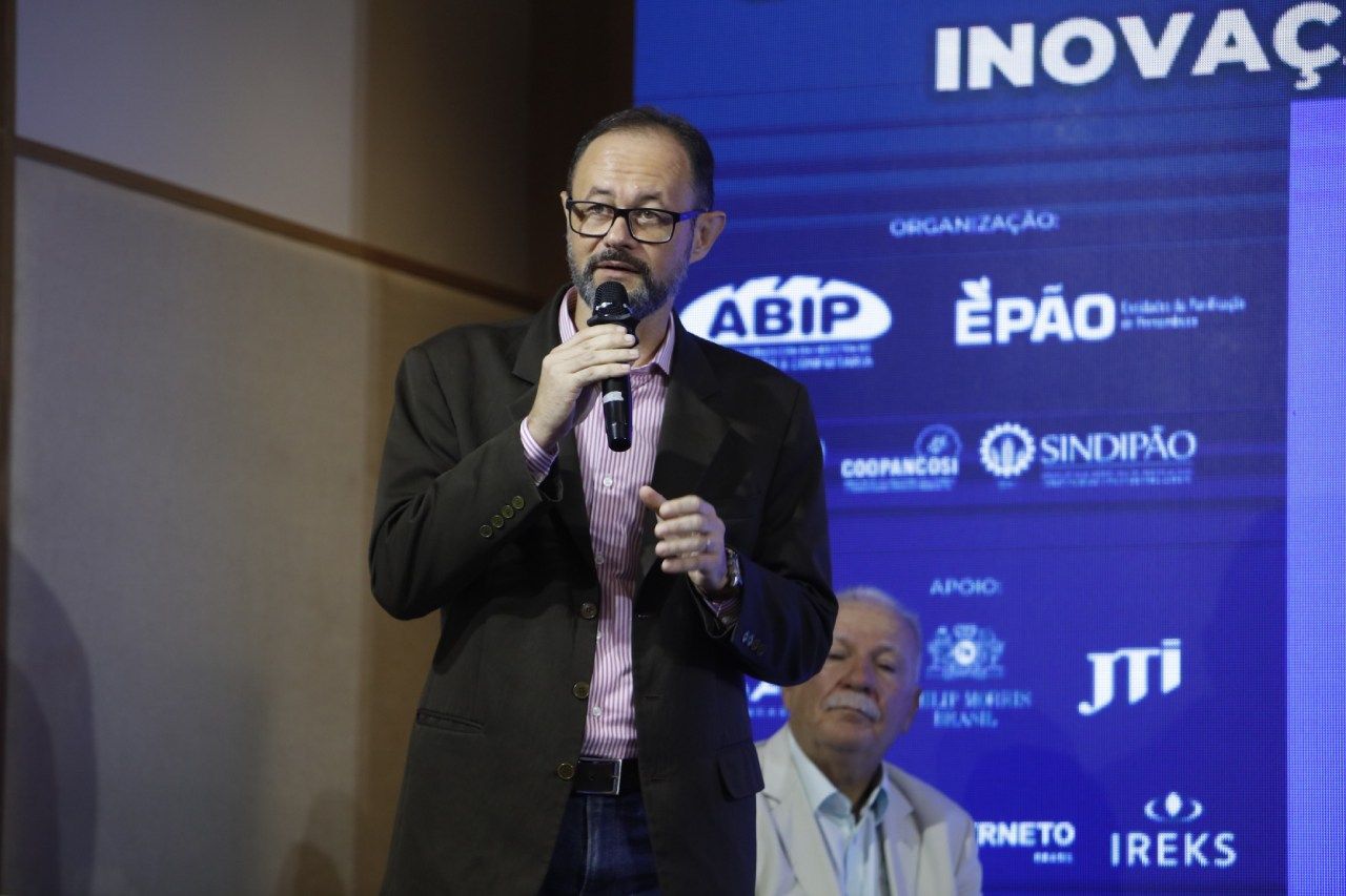 Um homem está falando em um microfone em frente a uma placa que diz inovac