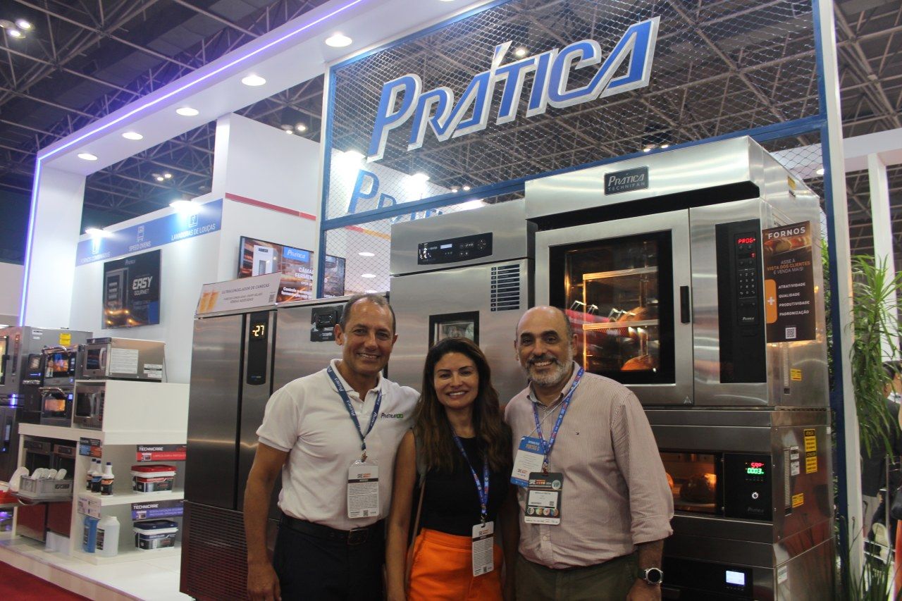 Três pessoas posam para uma foto em frente a uma máquina.