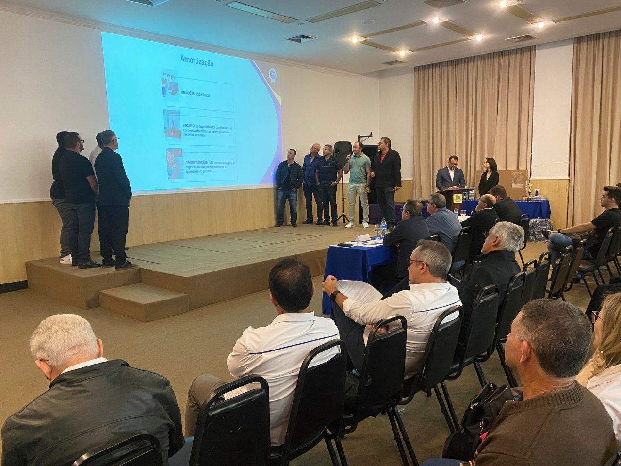 Um grupo de pessoas está sentado em uma sala assistindo a uma apresentação.