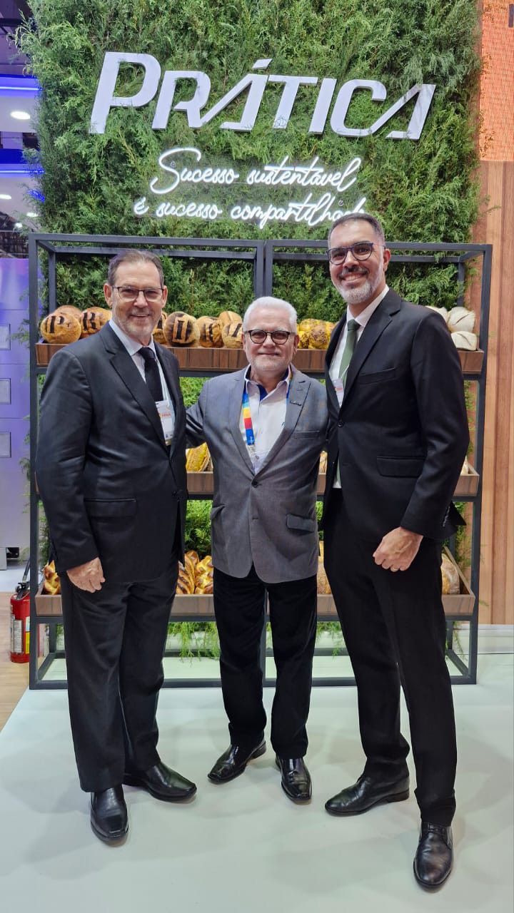 Três homens de terno estão posando para uma foto em frente a uma parede verde.