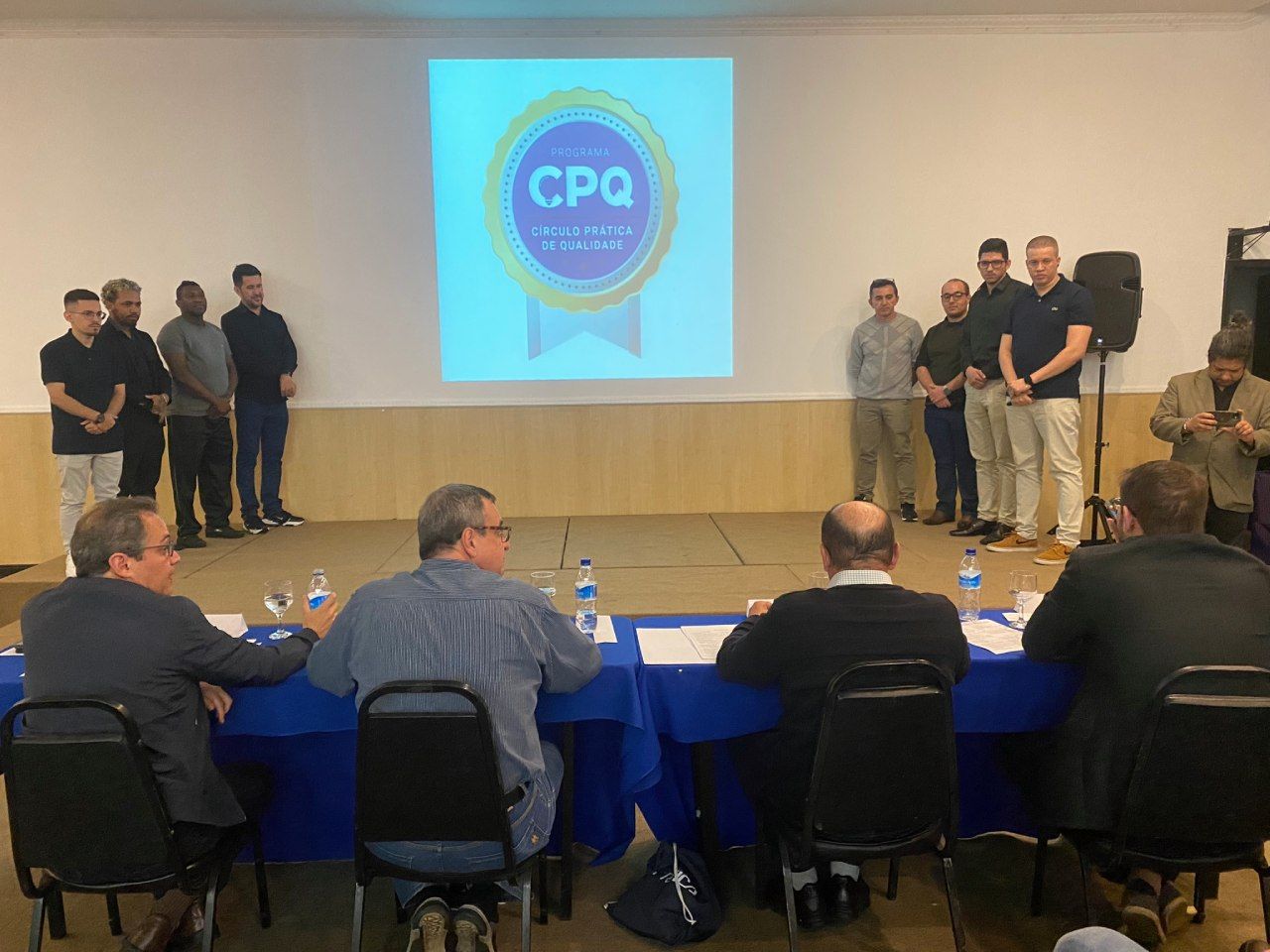 Um grupo de homens está sentado em mesas em frente a uma tela de projetor.