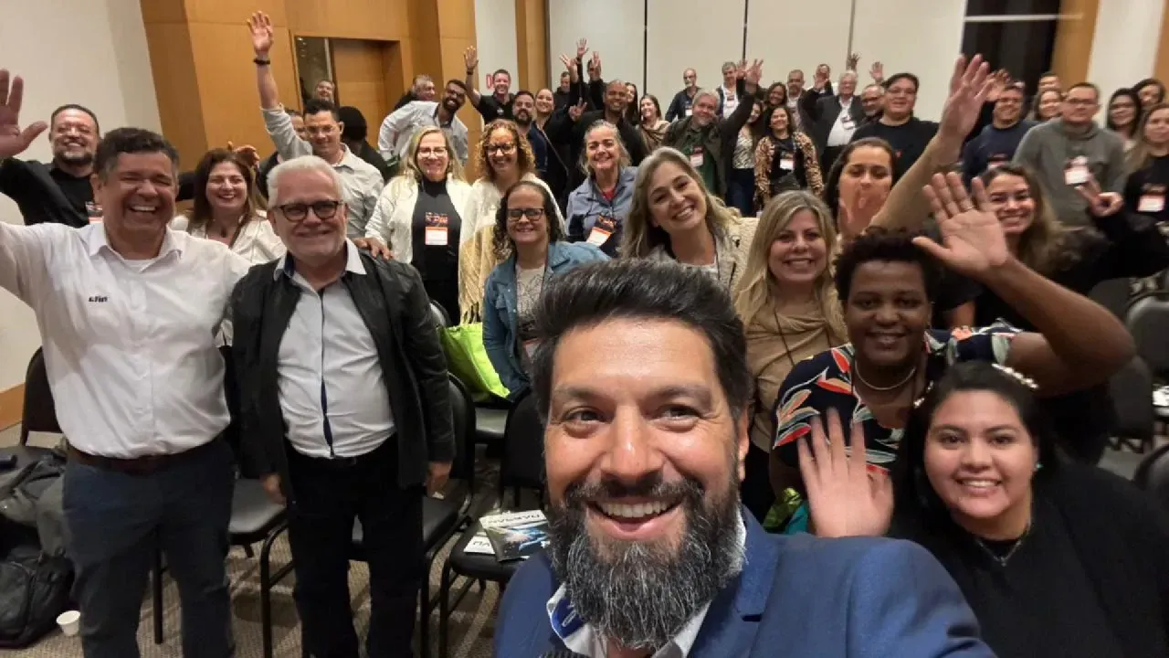 Um homem com barba está tirando uma selfie com um grupo de pessoas.