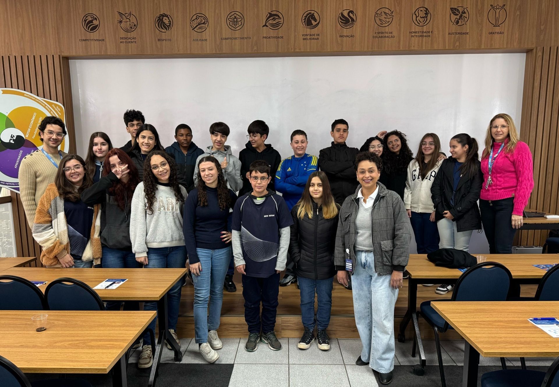 Grupo de alunos e professores posam juntos em uma sala de aula, sorrindo.