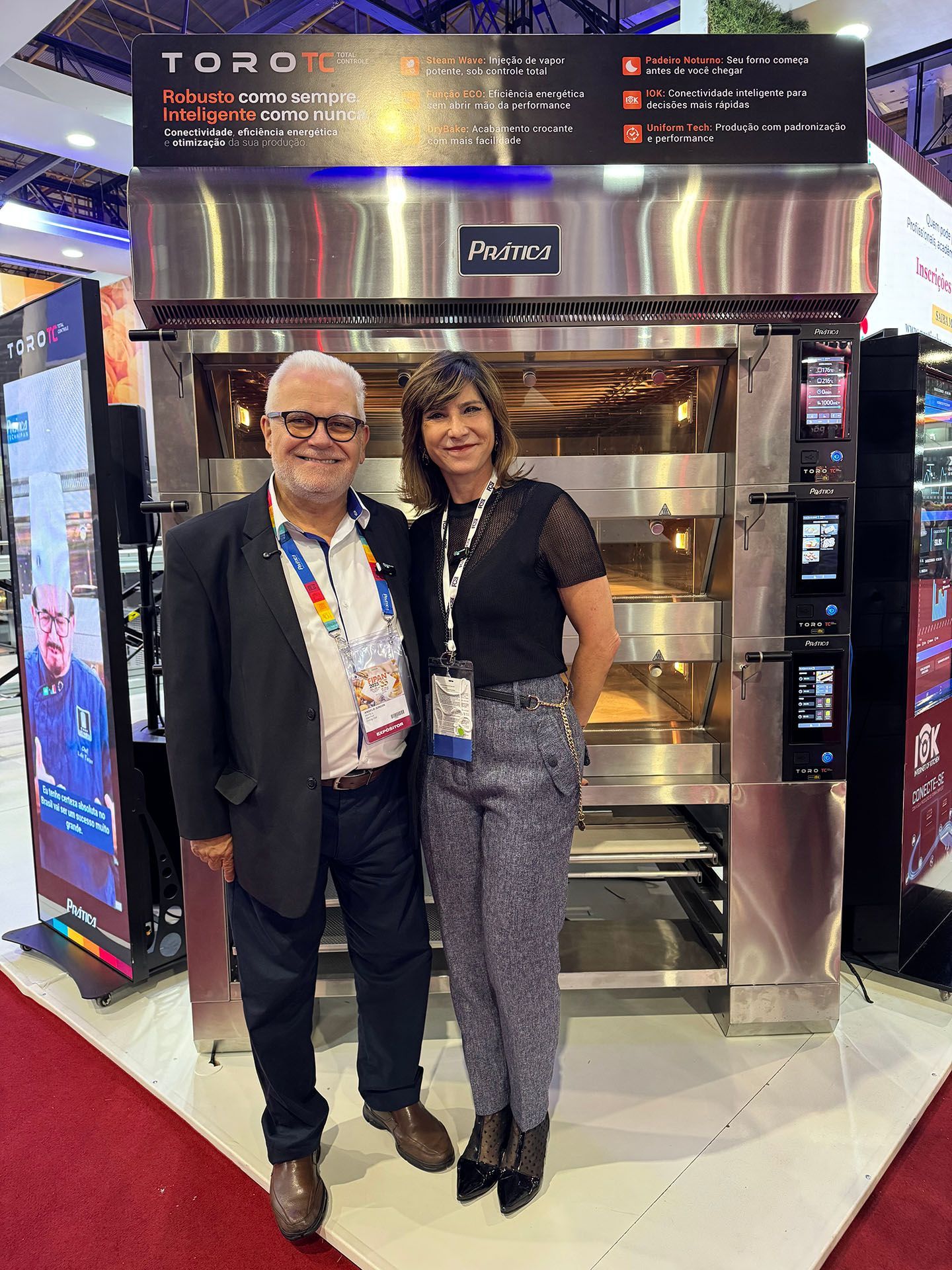 Um homem e uma mulher estão posando para uma foto em frente a um forno.