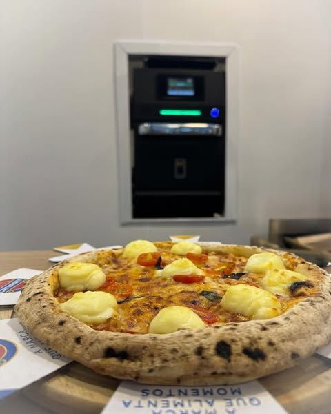 Uma pizza está sobre uma mesa de madeira em frente a um caixa eletrônico