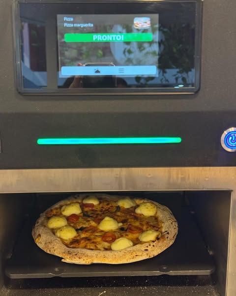 Uma pizza está sendo preparada em uma máquina que diz pronto na tela