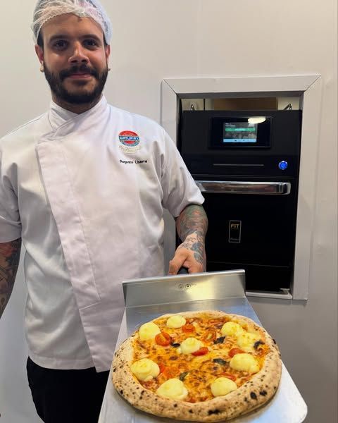 Um chef está segurando uma pizza na frente de uma máquina
