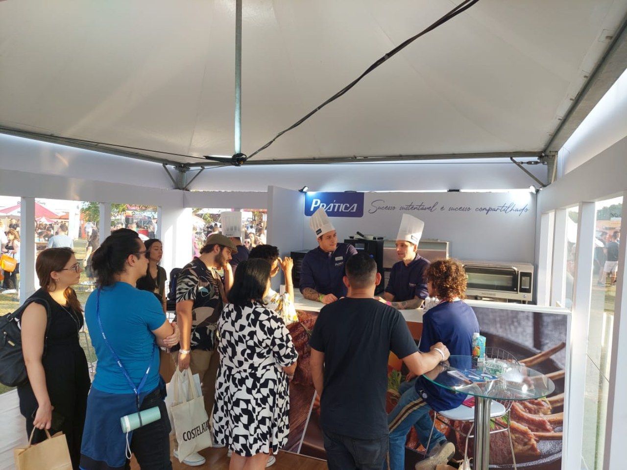 Um grupo de pessoas está em pé ao redor de uma mesa em uma tenda.