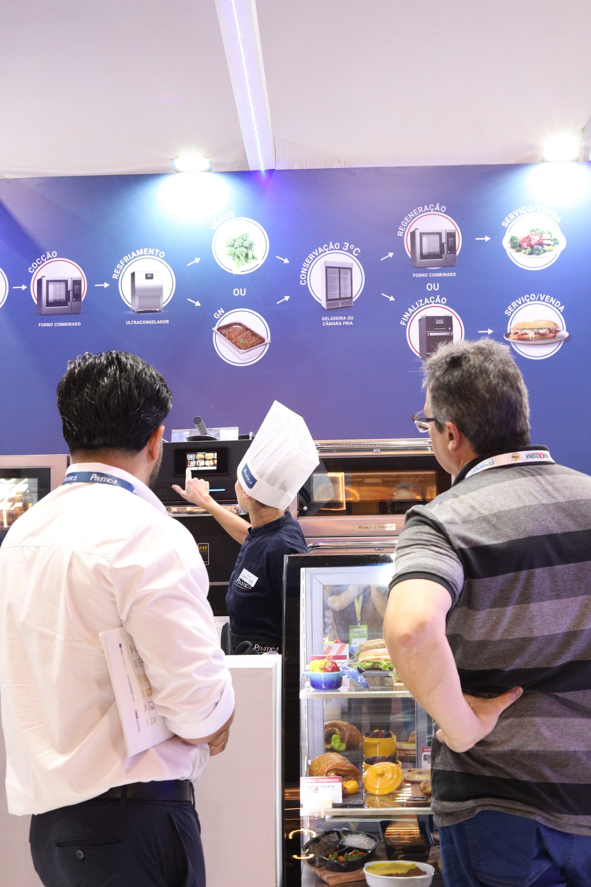 Um homem com chapéu de chef está parado em frente a uma vitrine de comida.