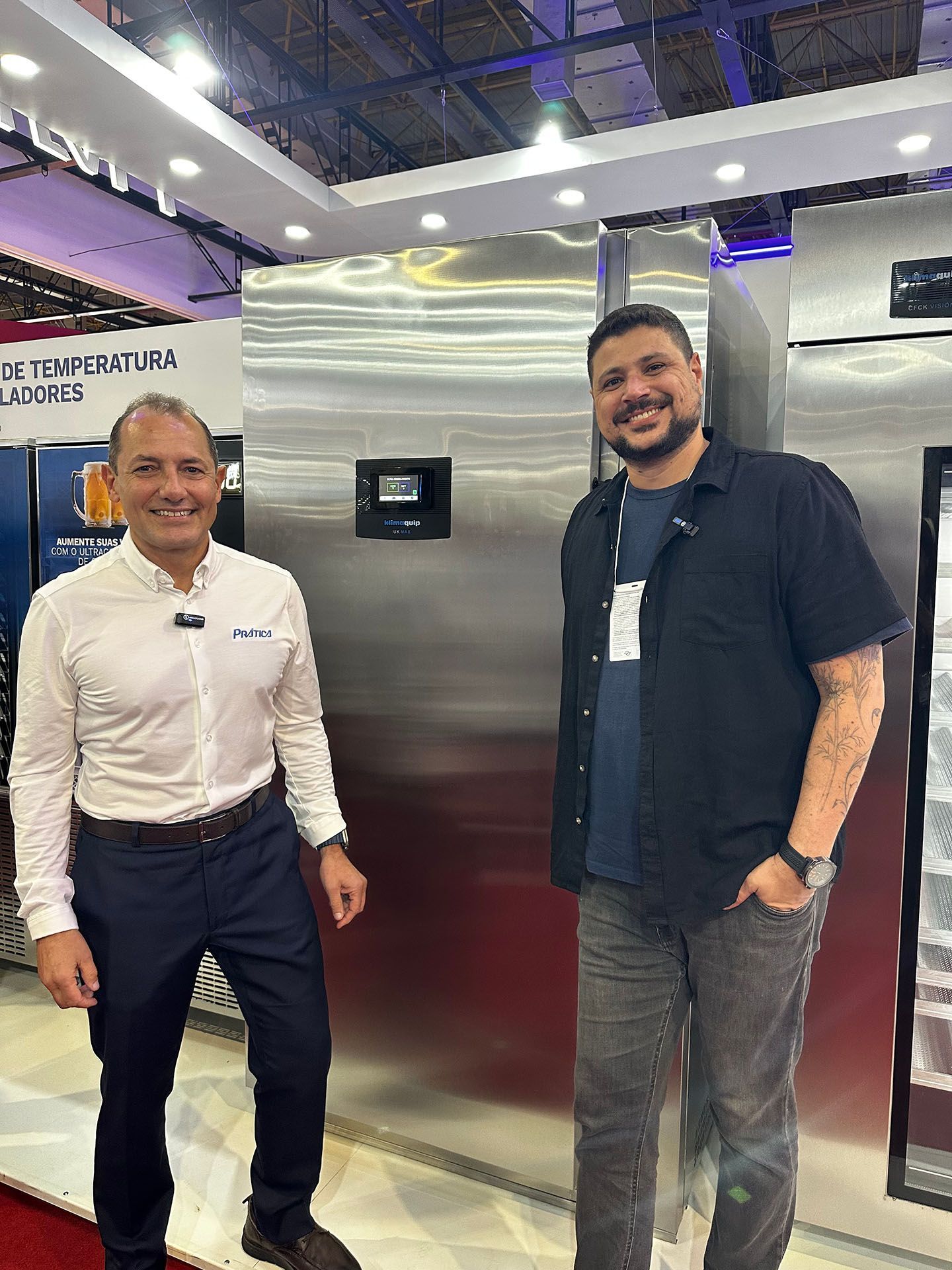 Dois homens estão parados um ao lado do outro em frente a uma geladeira.
