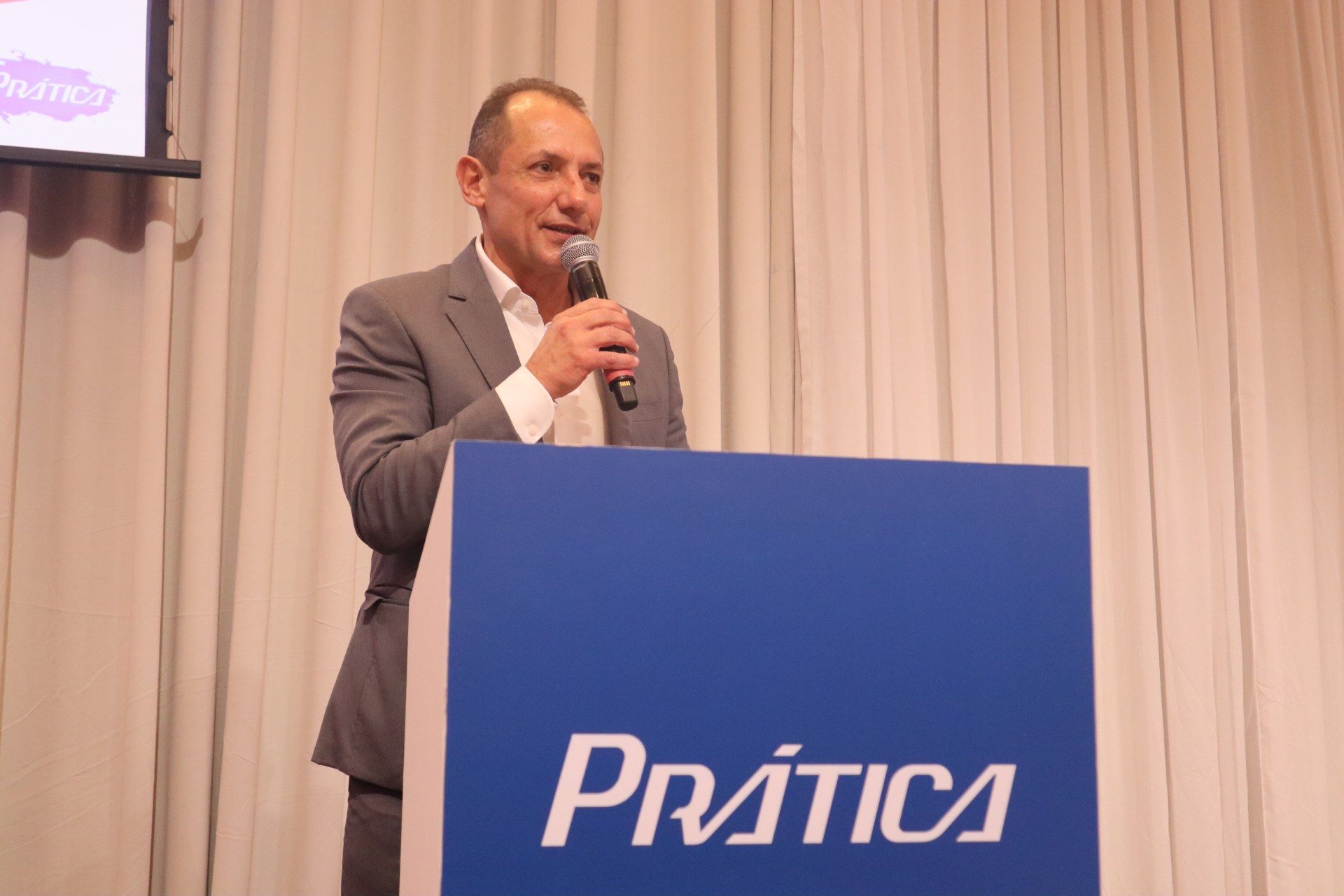 Um homem de terno está em pé no pódio segurando um microfone.