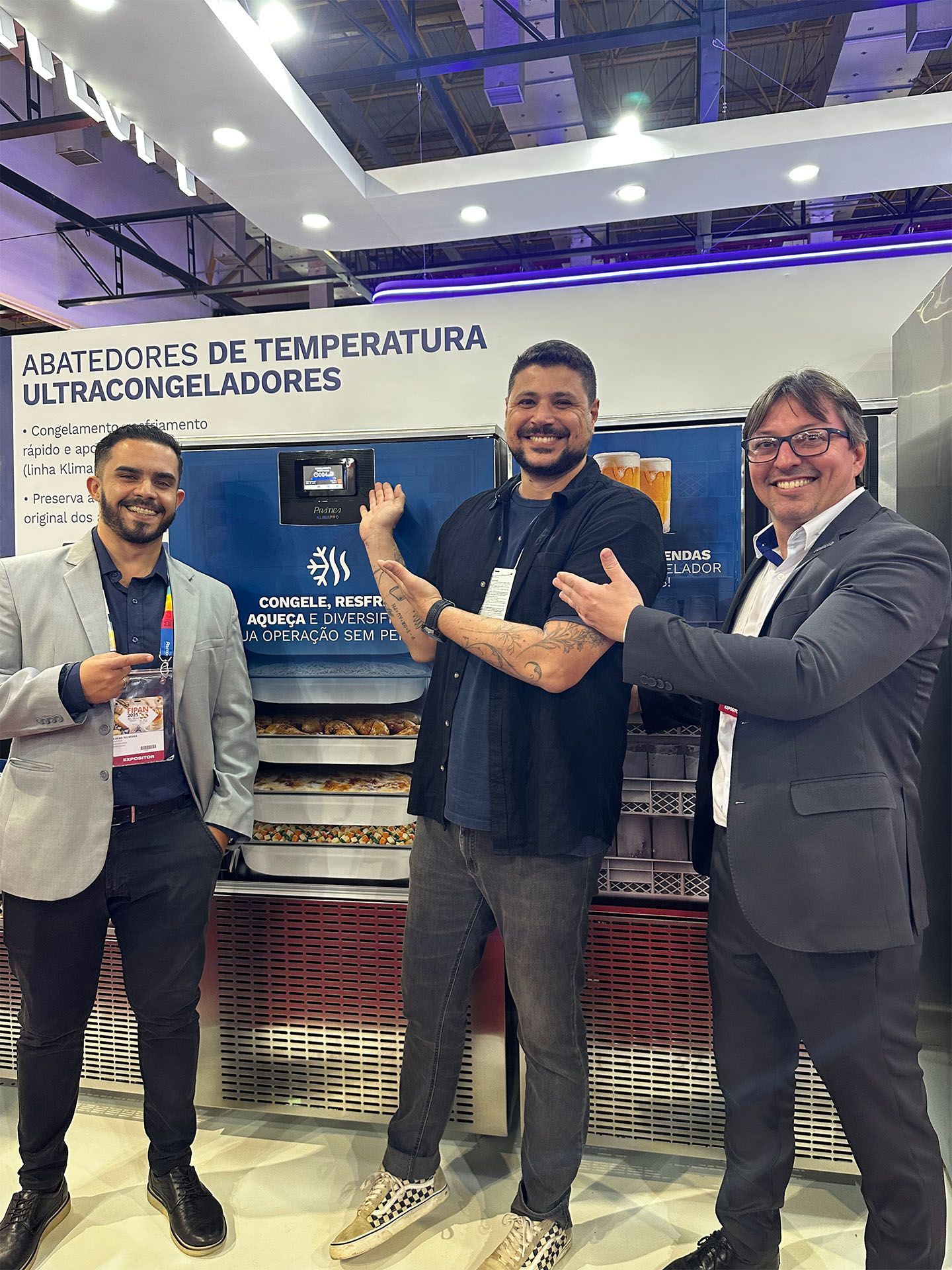 Três homens estão parados um ao lado do outro em frente a uma geladeira.