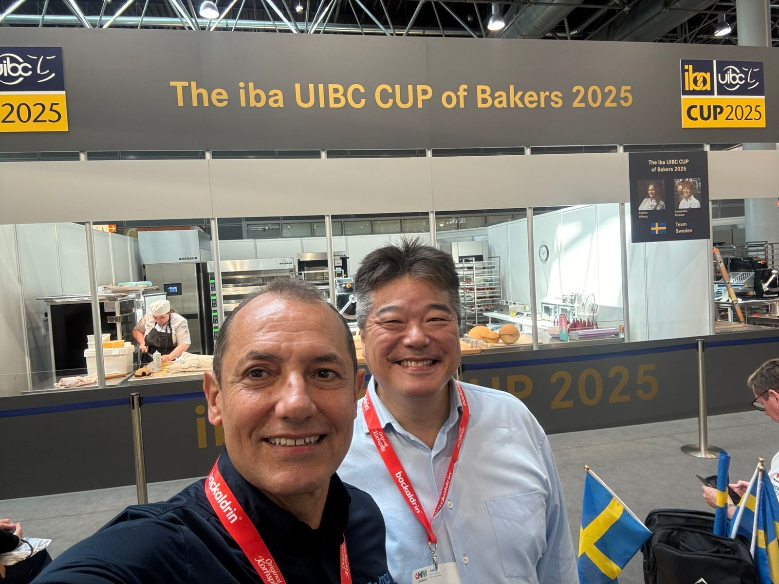 Dois homens estão posando para uma foto em frente a uma placa que diz: Copa UIBC de Padeiros 2025.