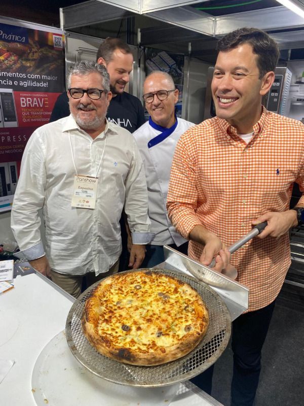 Um grupo de homens está em volta de uma pizza na cozinha.