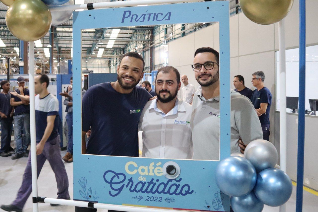Três homens estão posando para uma foto em frente a uma placa que diz café gratidao