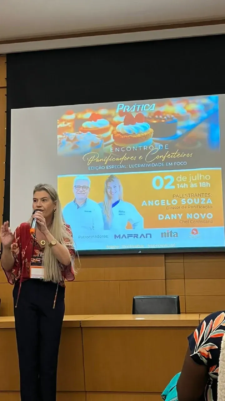 Uma mulher está fazendo uma apresentação em frente a uma tela grande.