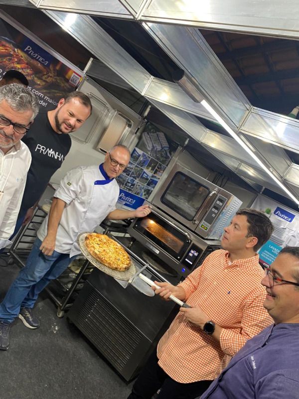 Um grupo de homens está em volta de uma pizza na cozinha.