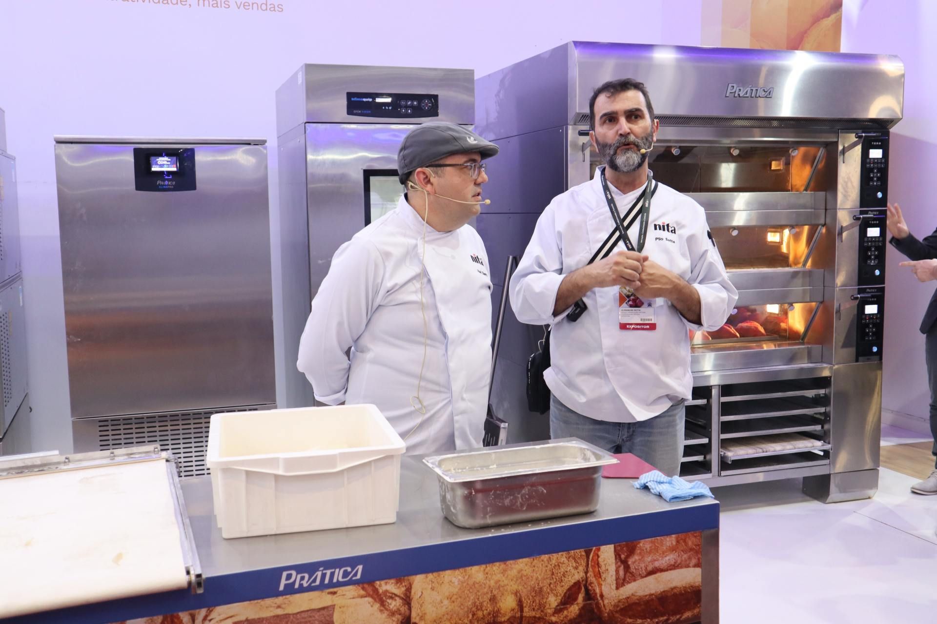 Dois homens estão de pé, um ao lado do outro, em frente a um forno.