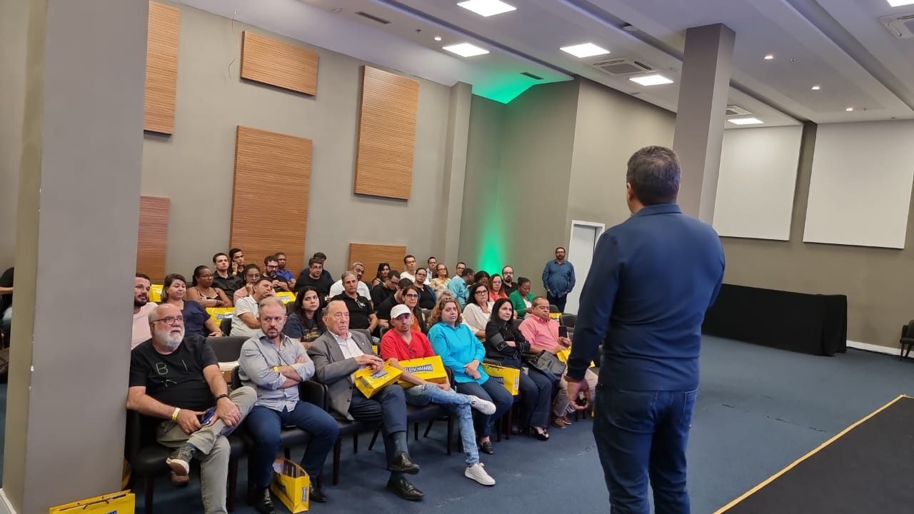 Um homem está em pé na frente de um grande grupo de pessoas em uma sala de conferências.