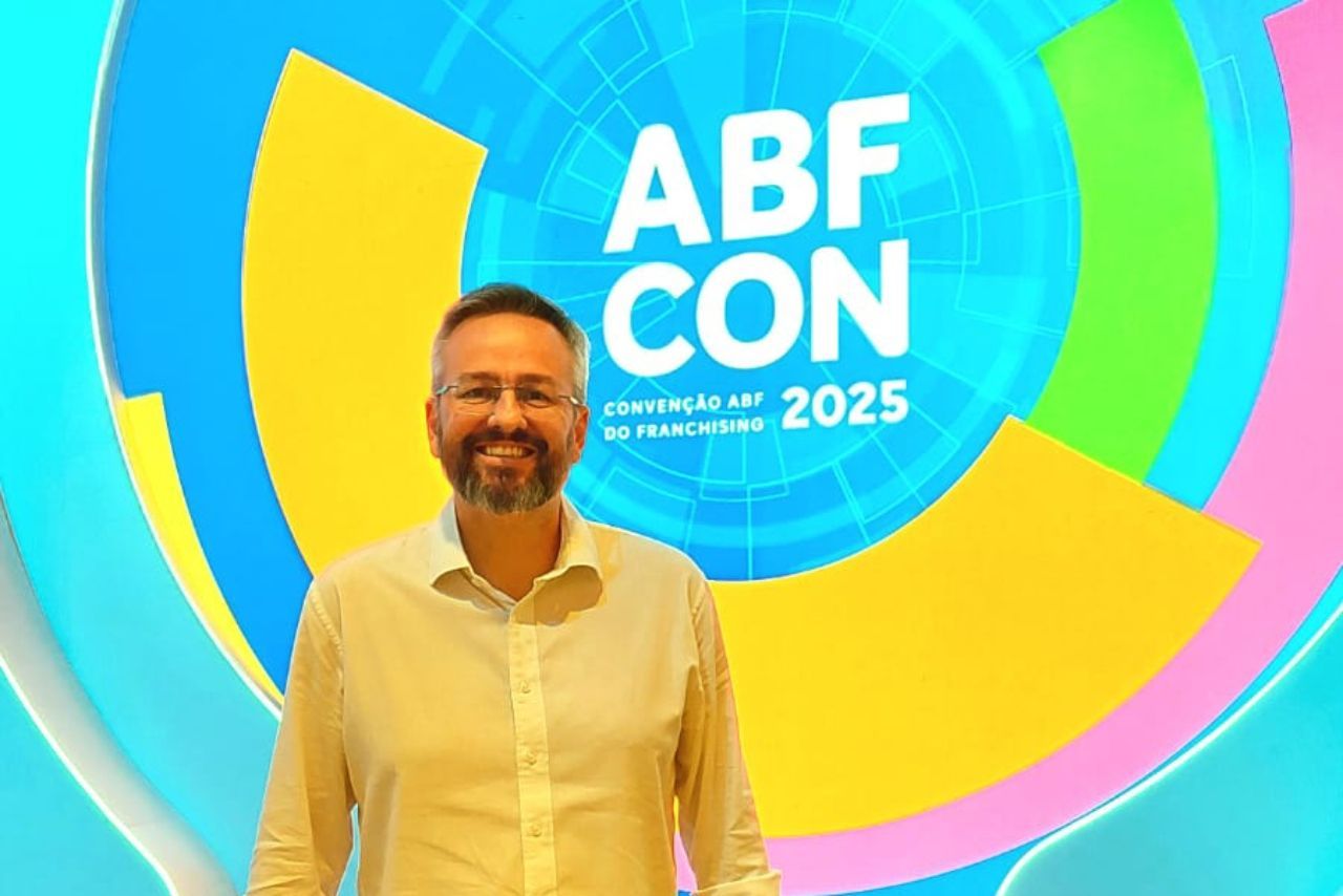 Homem de camisa clara sorri em frente a um cenário colorido