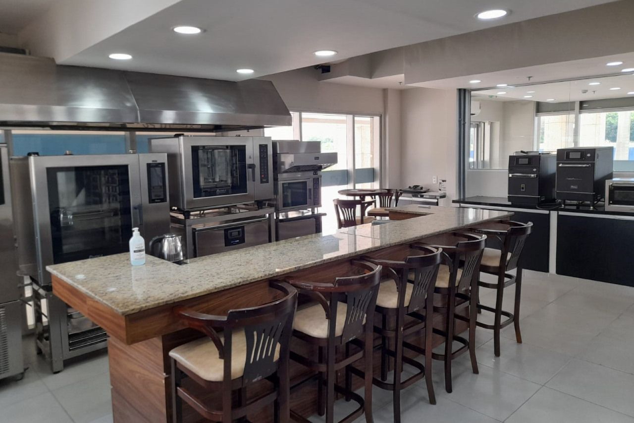 Uma cozinha com um balcão longo, bancos e muitos eletrodomésticos.