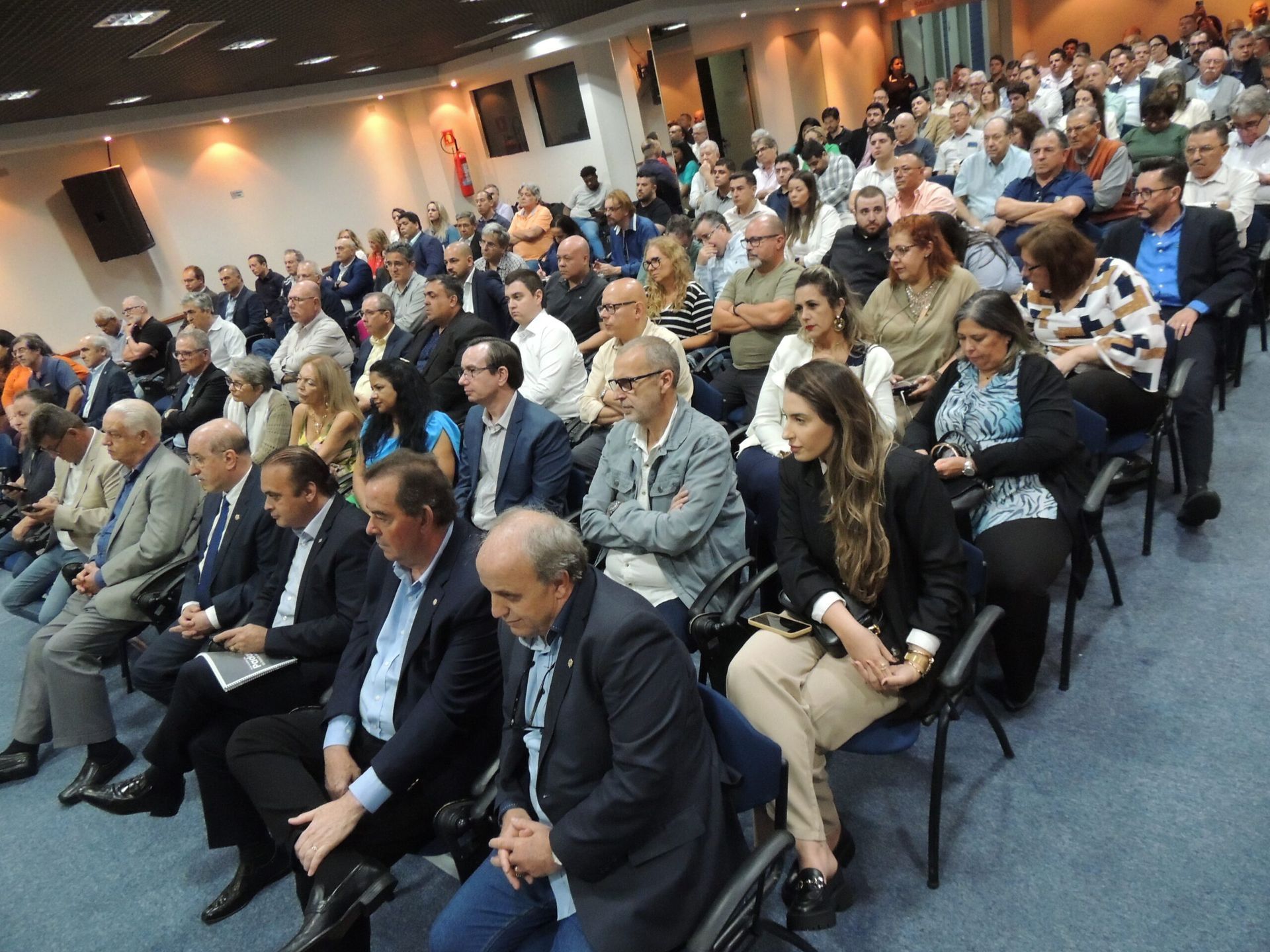 Um grande grupo de pessoas está sentado em cadeiras em uma sala.
