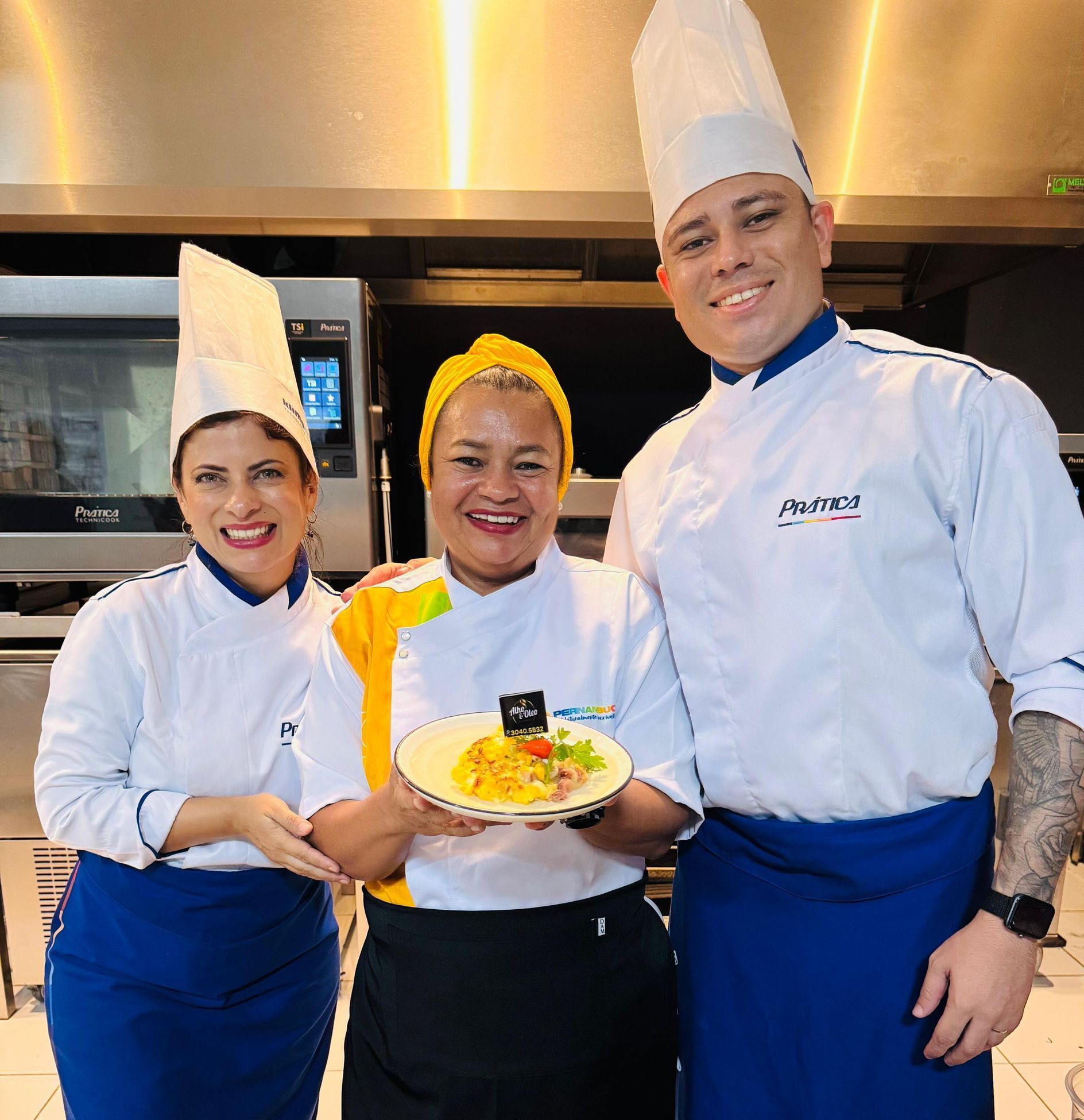 Três chefs estão posando para uma foto e um deles está segurando um prato de comida