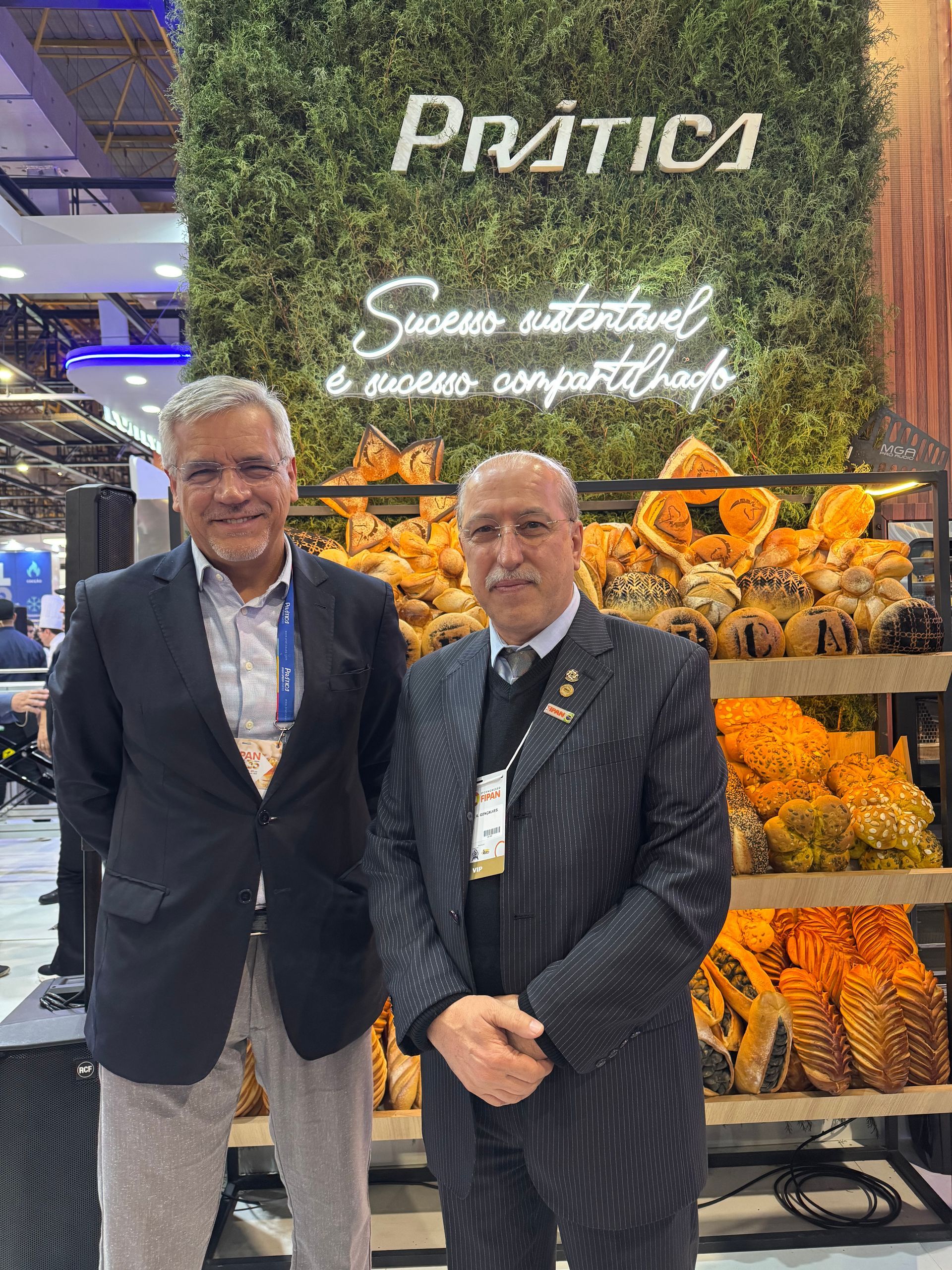Dois homens de terno estão parados um ao lado do outro em frente a uma exposição de comida.