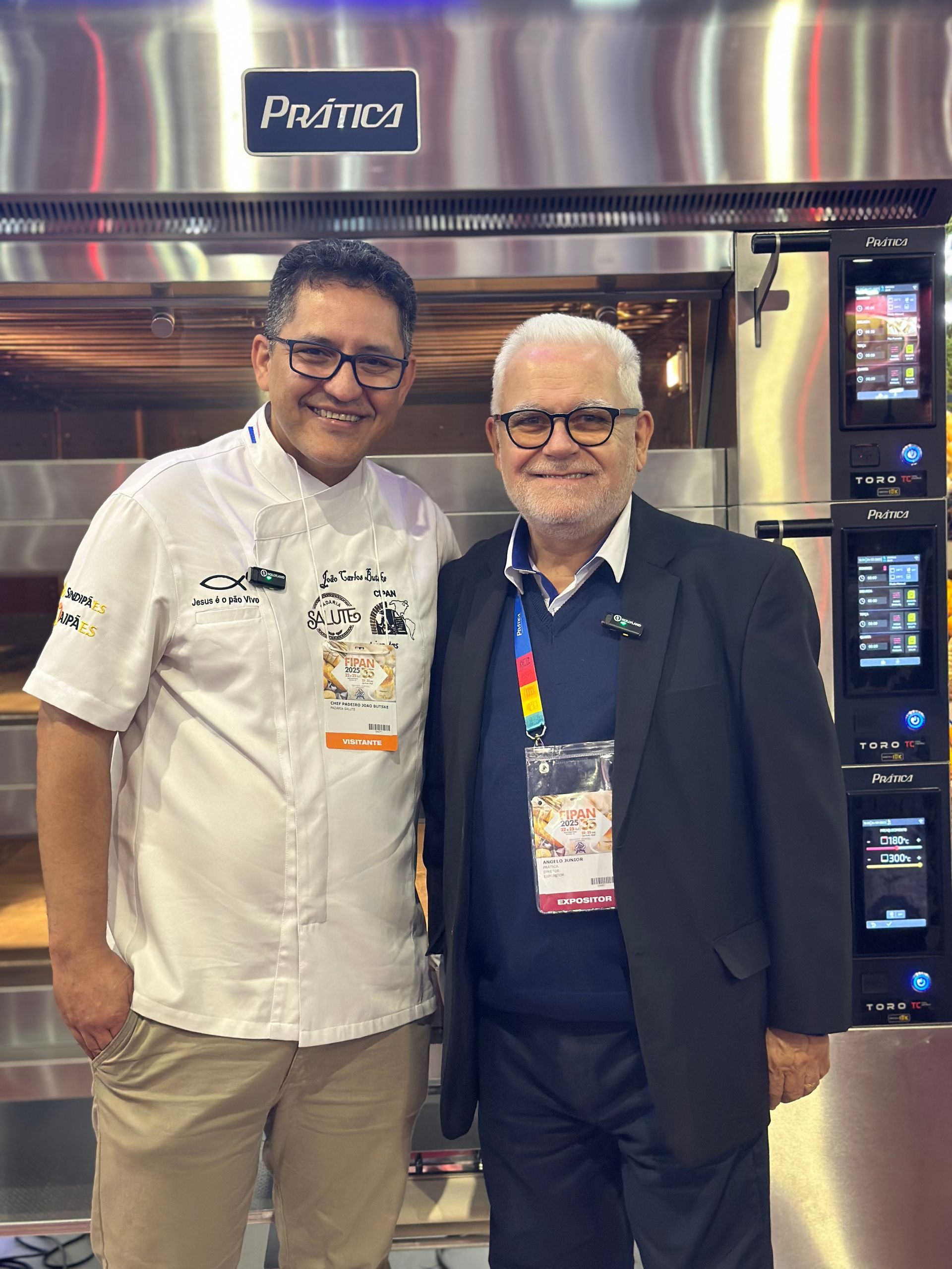 Dois homens posando para uma foto em frente a um forno de aço inoxidável.