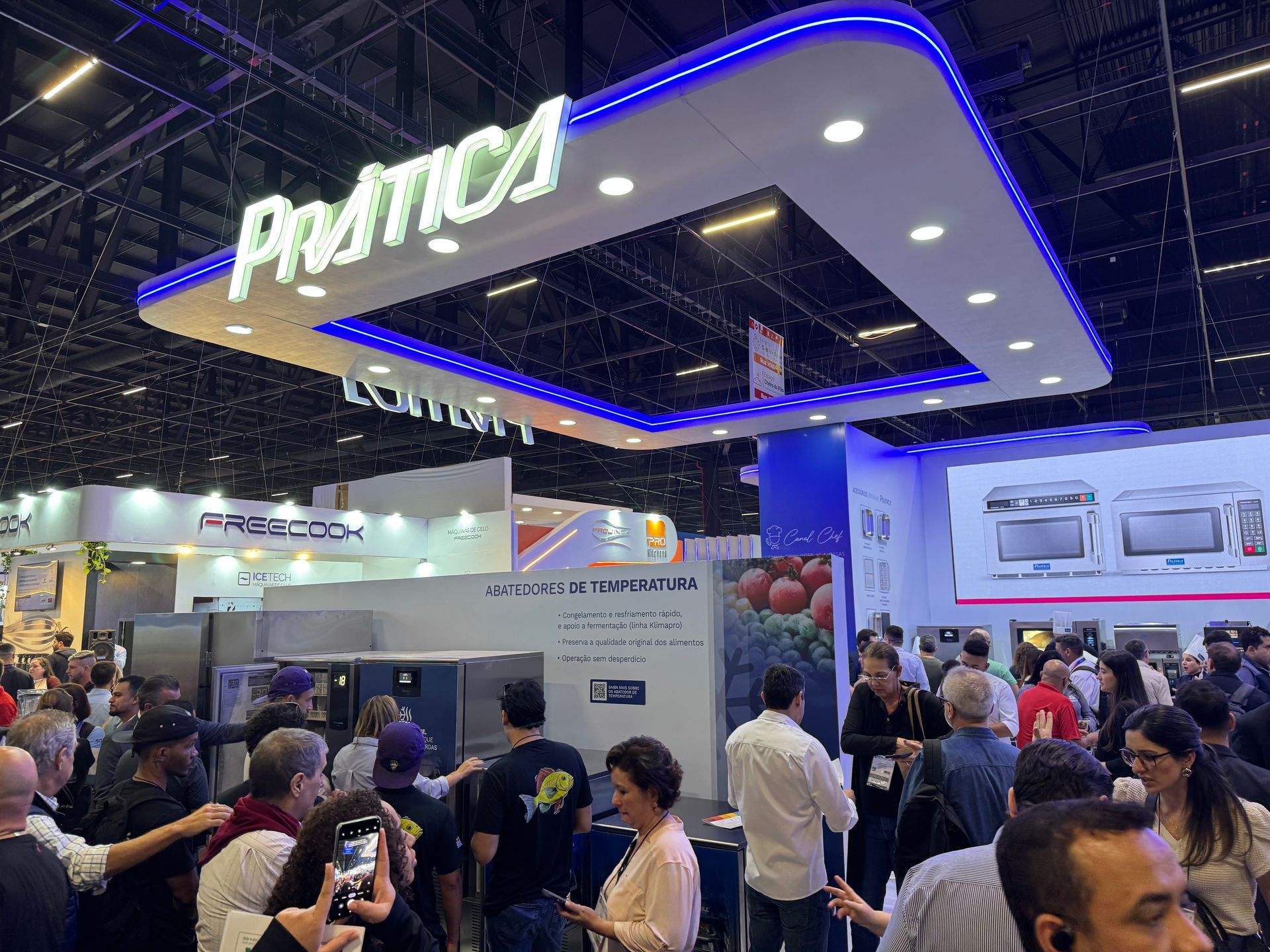 Uma multidão de pessoas reunidas ao redor de um estande em uma feira comercial.