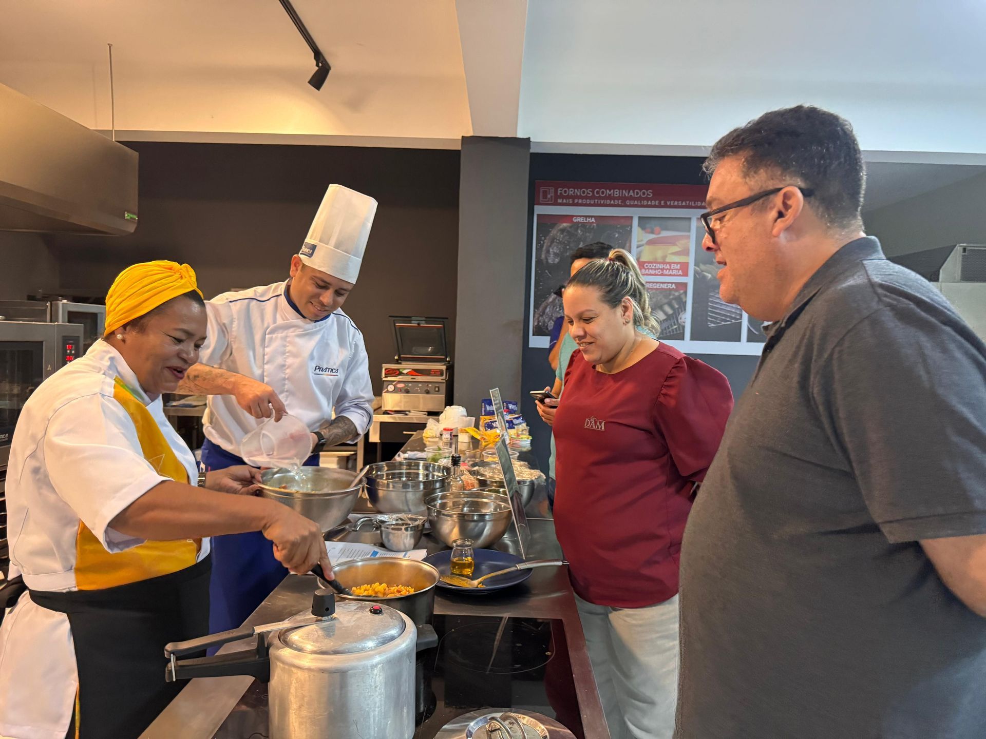 Um grupo de pessoas está em volta de uma mesa na cozinha observando um chef cozinhar.
