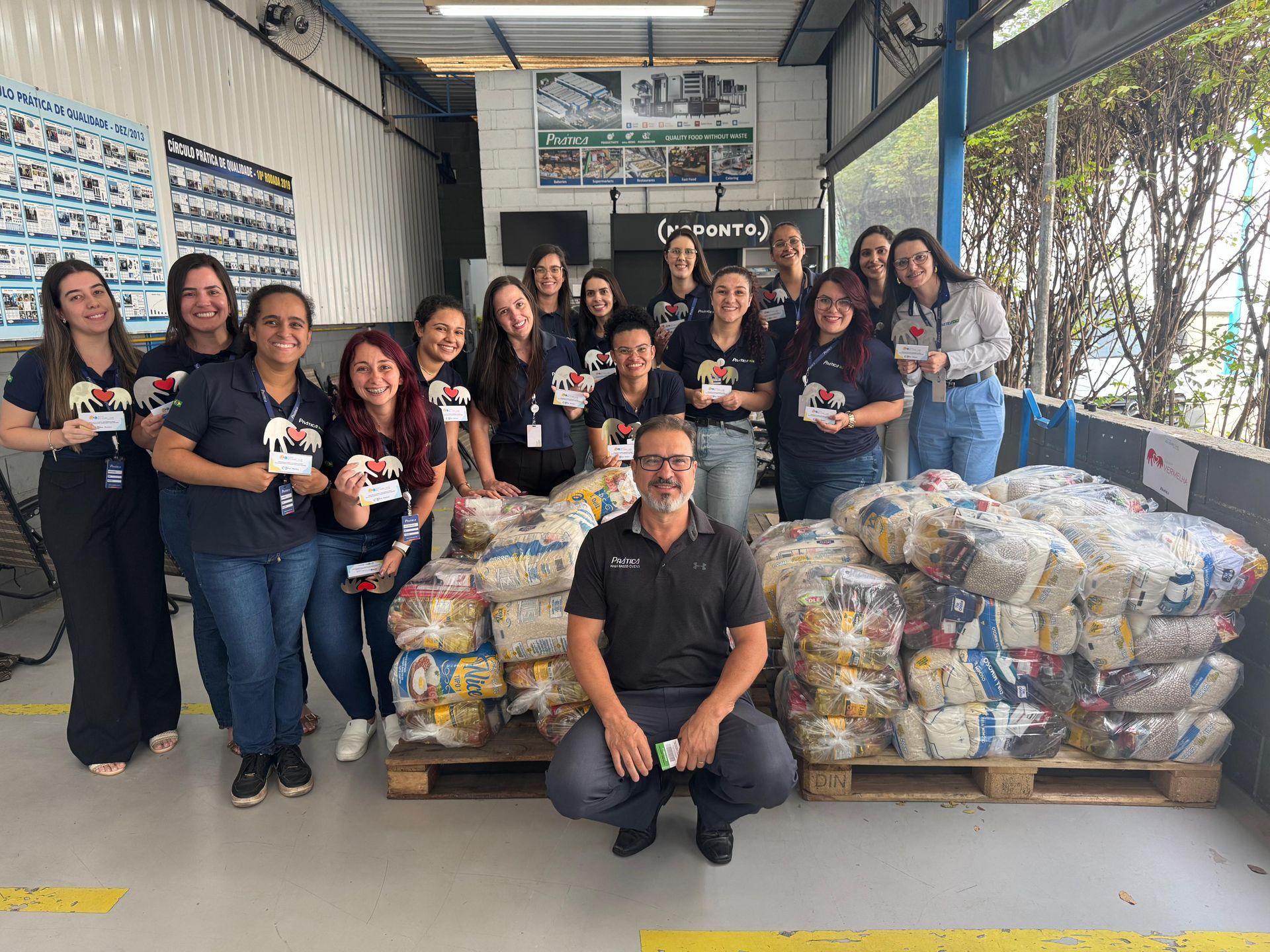 Grupo de pessoas posa com pilhas de doações de alimentos.