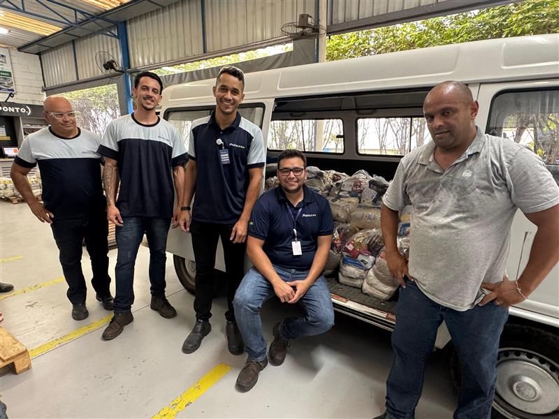 Cinco pessoas em pé perto de uma van carregada de sacolas. Os homens vestem camisas azuis e pretas.