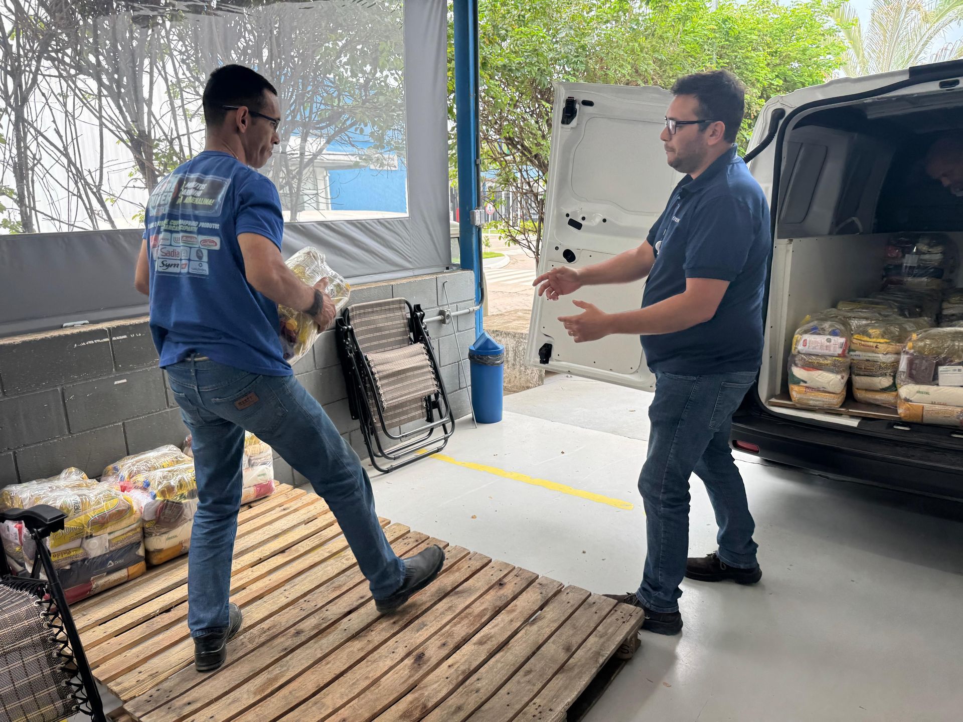 Dois homens carregam mercadorias embaladas de um palete para uma van. Um homem carrega as mercadorias.