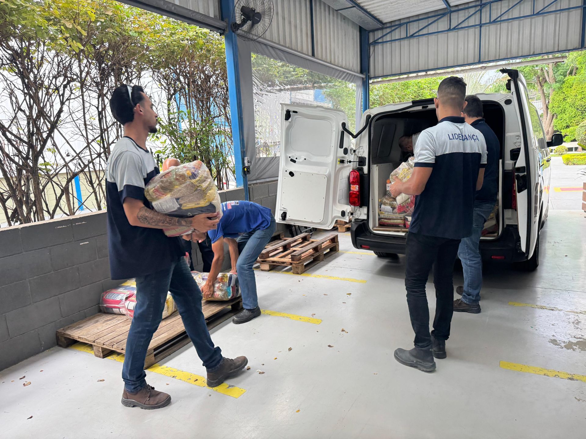 Homens carregando pacotes em uma van branca em um armazém.