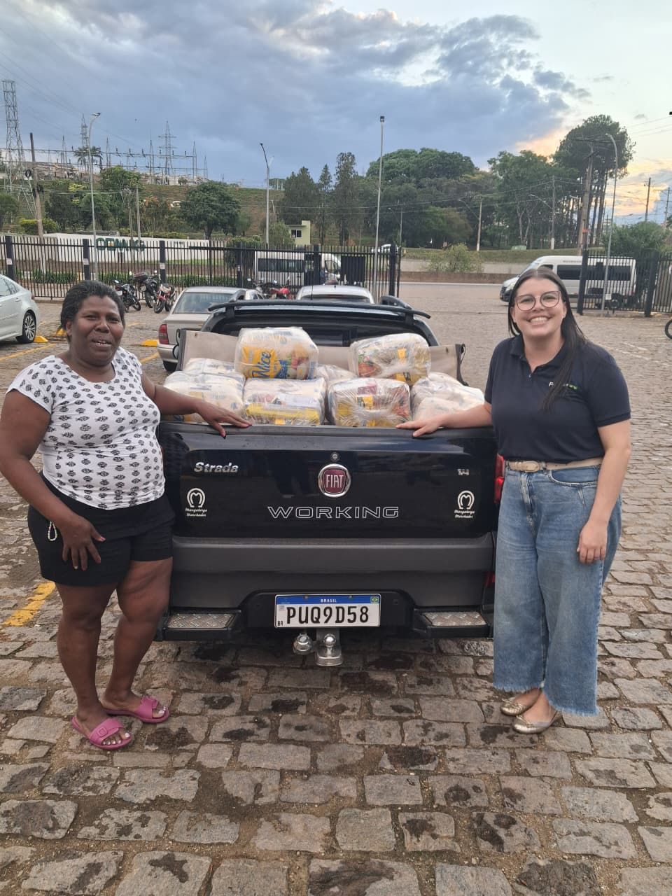 Duas mulheres perto da caçamba de um caminhão cheio de pacotes de comida. Elas sorriem.